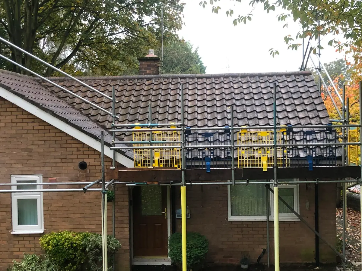 The same bungalow roof after cleaning, bare concrete tiles, same scaffold in place.