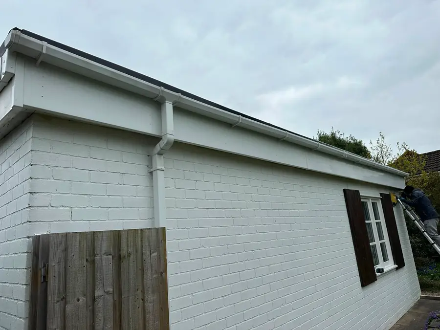 A newly fitted white fascia, soffit and gutter run on a painted brick bungalow.