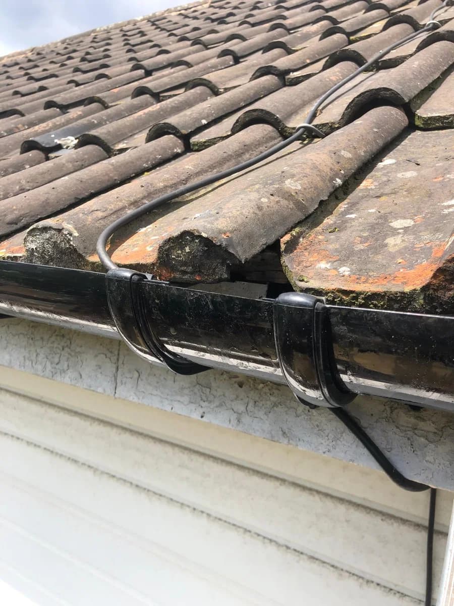 A black gutter run with a section come apart at the joint, under mossy roof tiles.