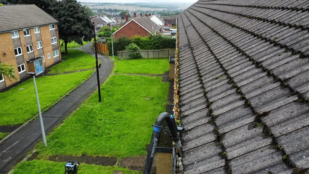 A wide view of a large roof with a leaf filled gutter run and the vacuum hose below.