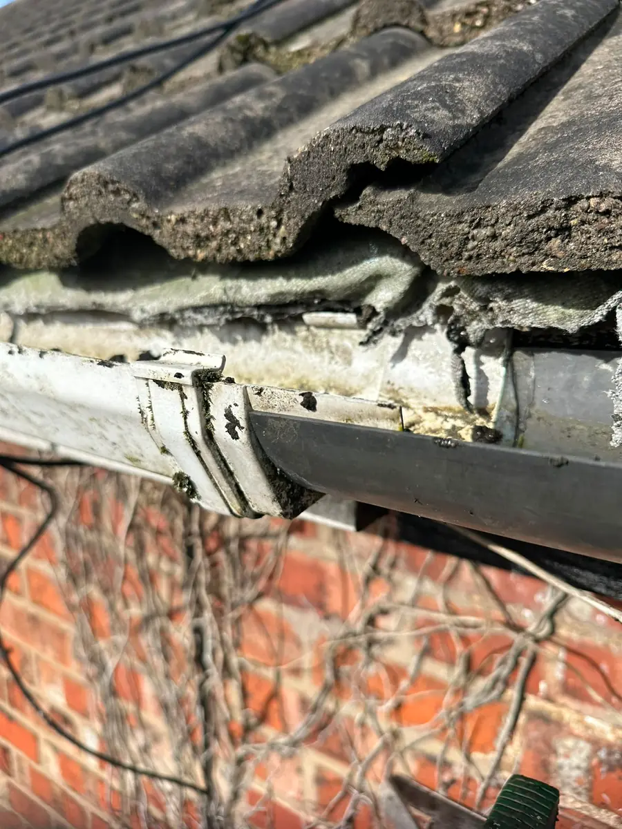 A failed plastic gutter joint with a rotted bracket behind it.